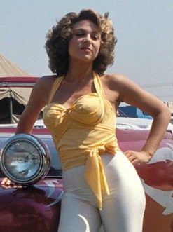 a woman standing next to a parked car in front of a red and white car