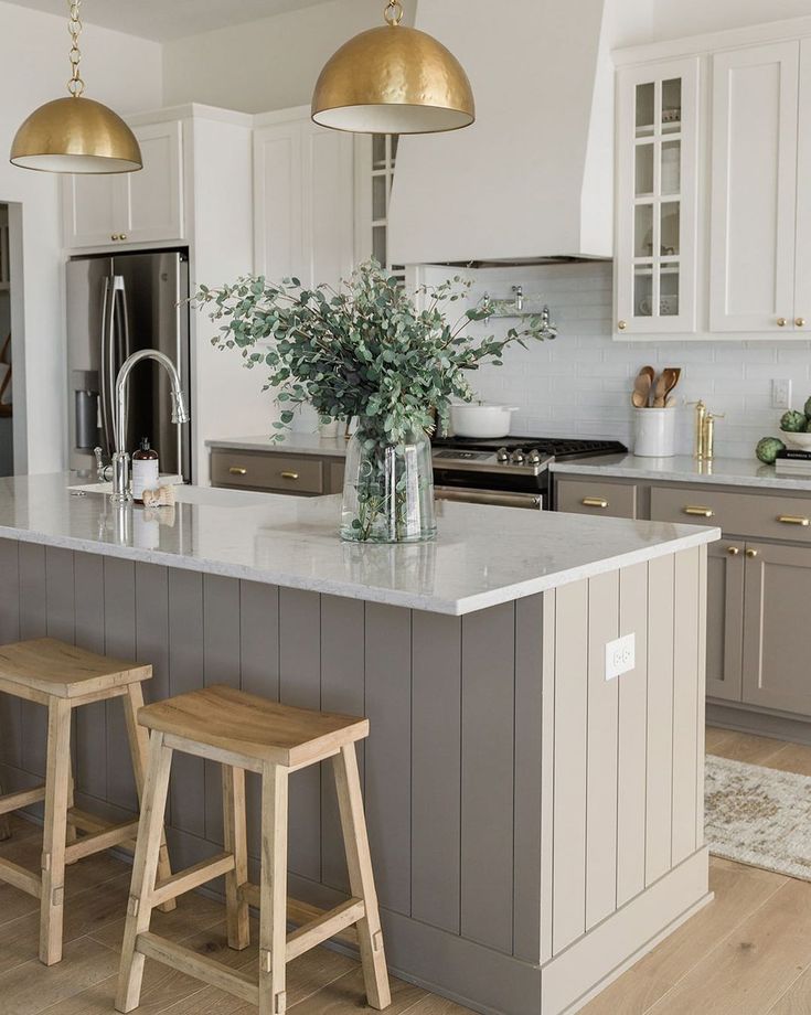 a large kitchen with two stools in front of the island and gold lights hanging from the ceiling