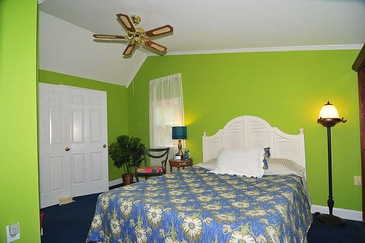 a bed room with a neatly made bed and a ceiling fan in it's corner