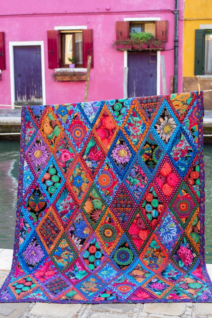 a multicolored quilt is displayed in front of a pink building