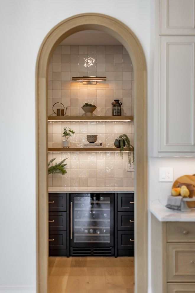 an arched doorway leads to a kitchen with white cabinets