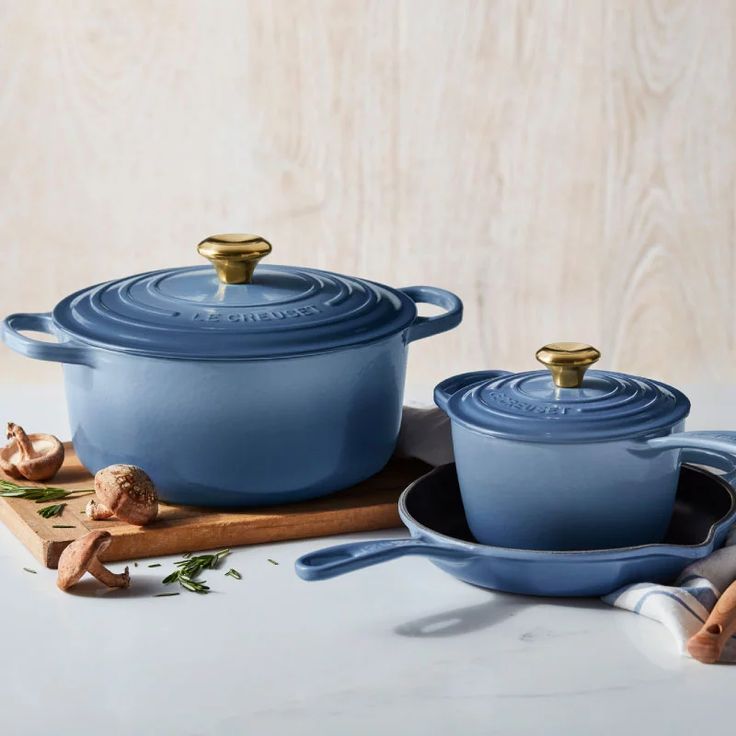 two blue casserole dishes with gold handles on a white countertop next to cinnamon sticks and spices