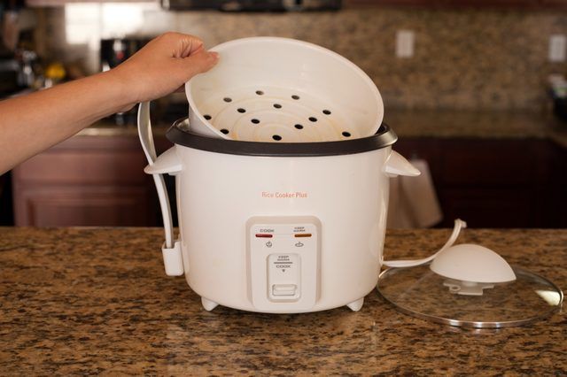 a person is holding the lid on an electric rice cooker while it's being used