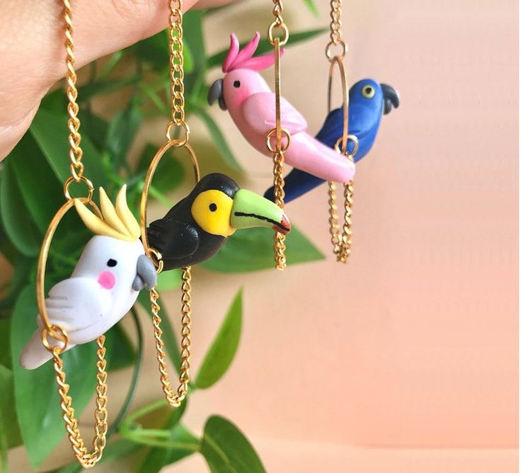 three birds with crowns on their heads are hanging from chains in front of a plant