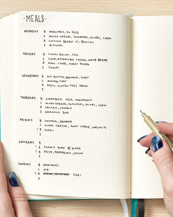 a person holding a pen and writing on a notebook with the words meals written in it