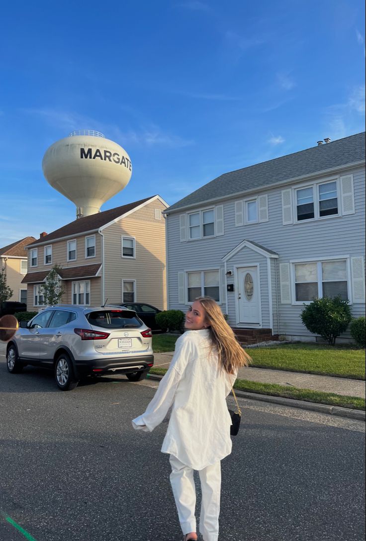 a woman is walking down the street in front of some houses and a water tower