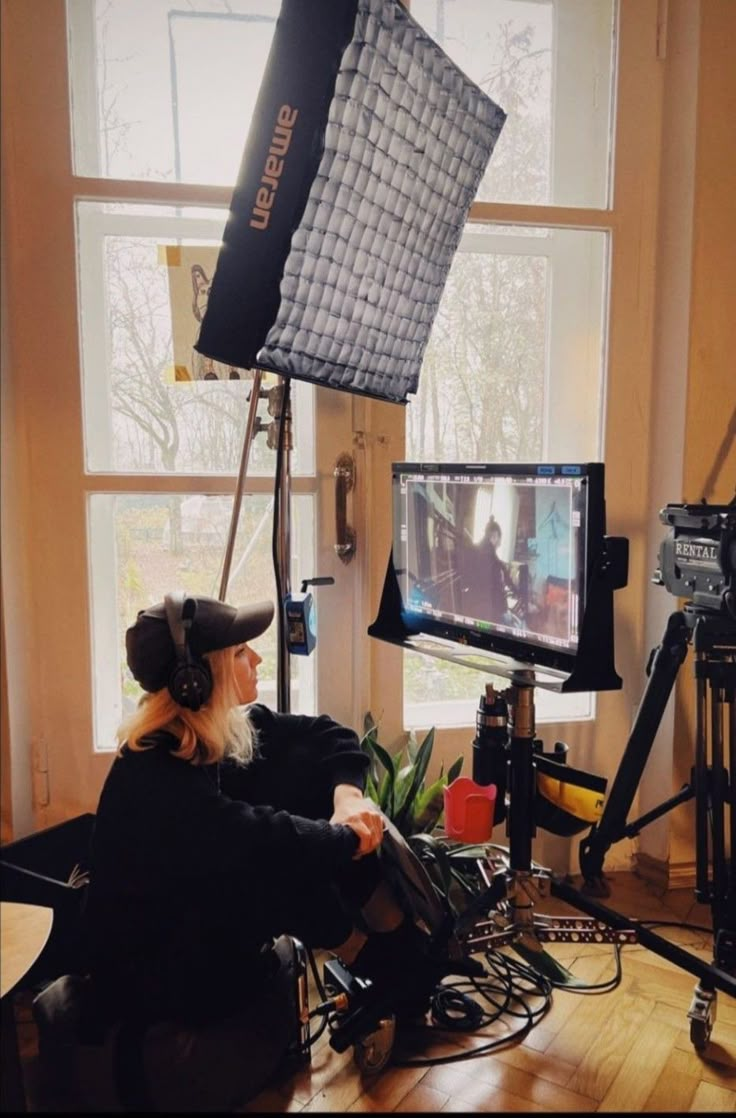 a person sitting in a chair with a camera and some lights on the floor next to a window