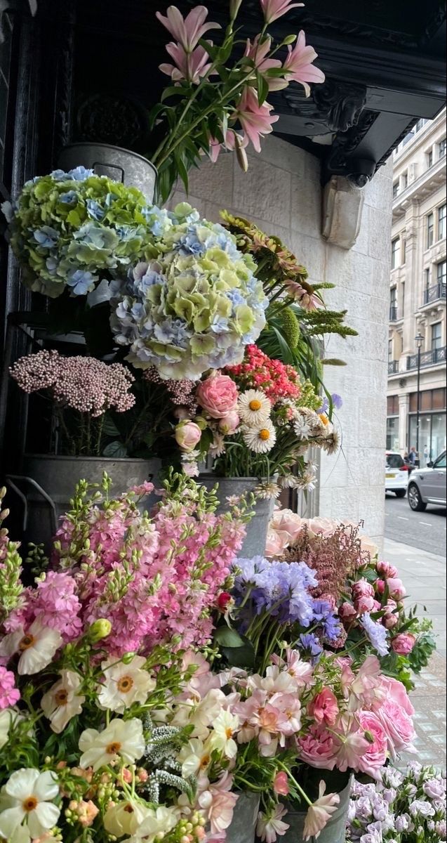 a bunch of flowers that are sitting on the side of a building with cars in the background