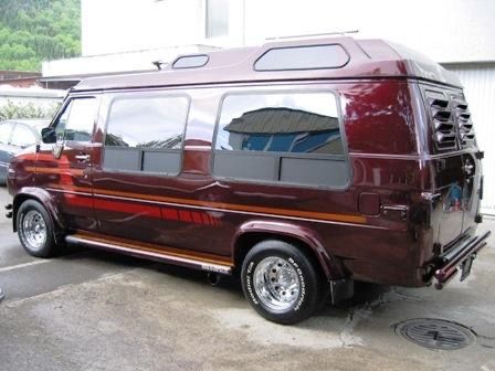 a maroon van parked in a parking lot next to other cars and people looking at it