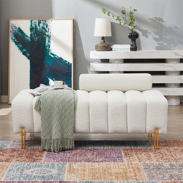 a white couch sitting on top of a wooden floor next to a painting and lamp