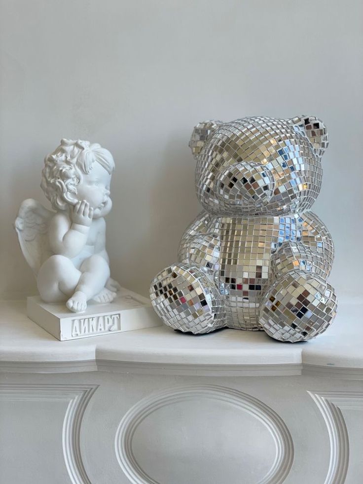 a white teddy bear sitting on top of a shelf next to a mirror ball sculpture