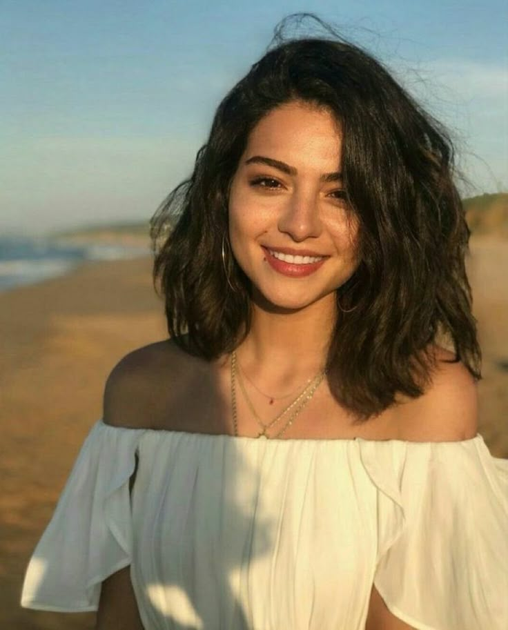 a woman standing on top of a sandy beach next to the ocean wearing a white shirt