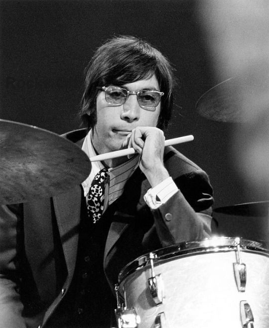 a man with glasses and a tie holding a drum in front of his face as he plays the drums