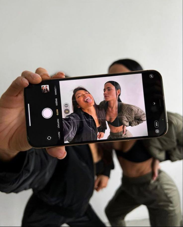 a person holding up a cell phone to take a selfie with two other people in the background