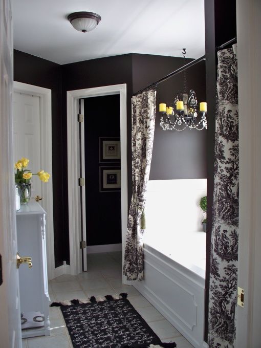 a bathroom with black walls and white flooring is decorated with yellow flowers in vases on the window sill