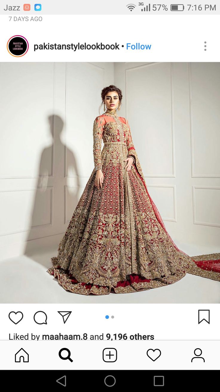 a woman standing in front of a white wall wearing a long dress with red and gold embroidery