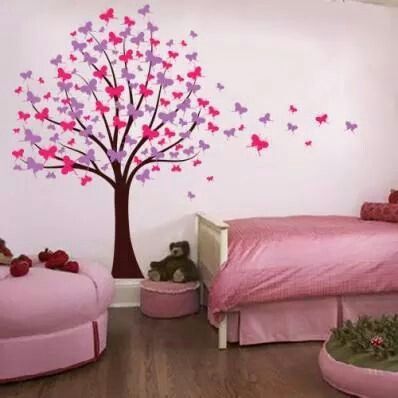 a pink bed room with butterflies on the tree wall decal and other items in front of it