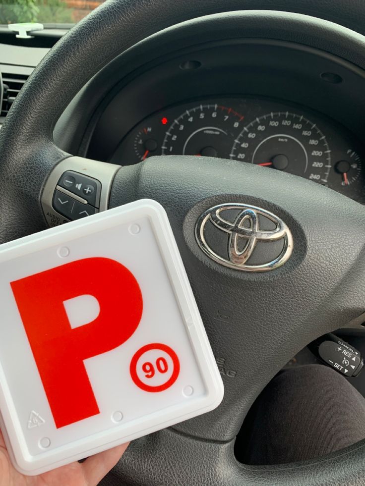 a person holding up a parking sign next to a steering wheel with the letter p on it