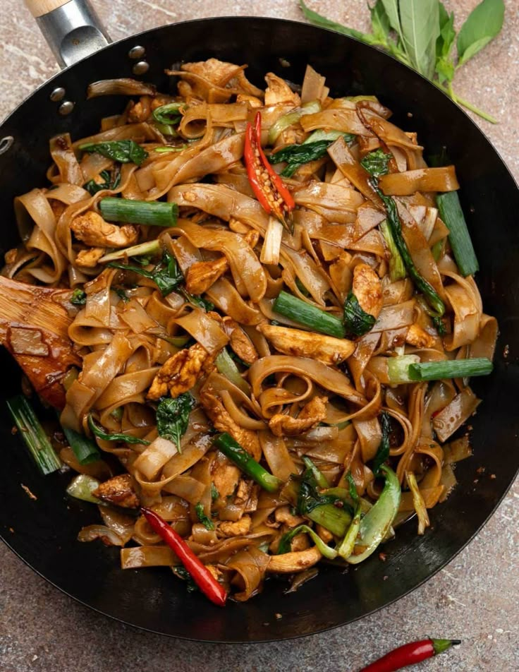 a wok filled with noodles and vegetables on top of a table next to red peppers