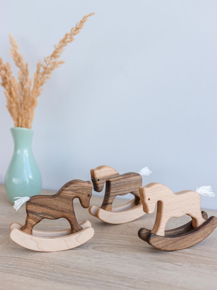 two wooden rocking horses on a table next to a vase with dried grass in it