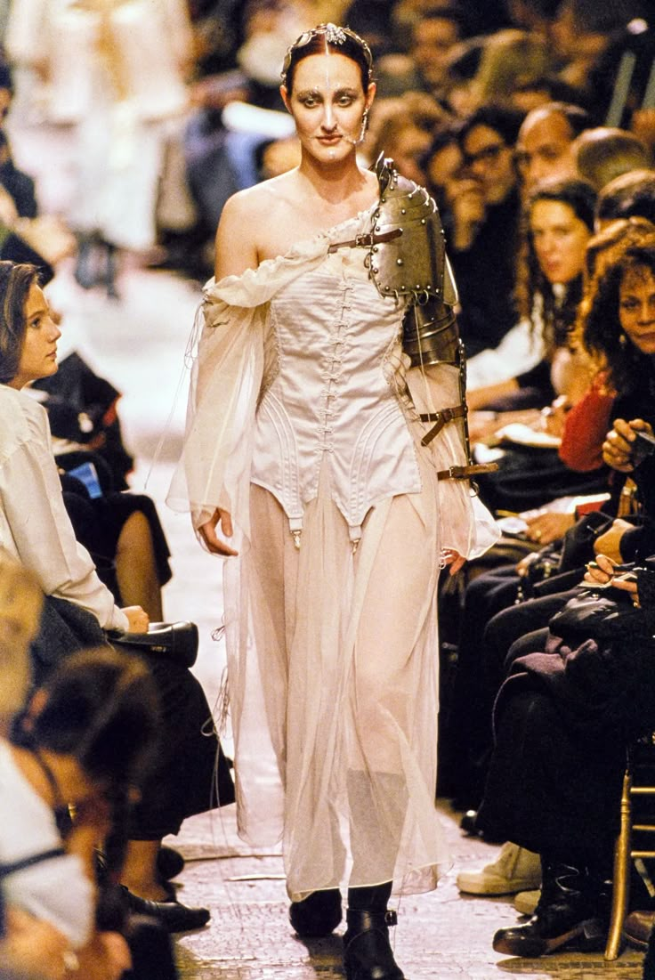 a woman is walking down the runway in a white dress with armor on her shoulders