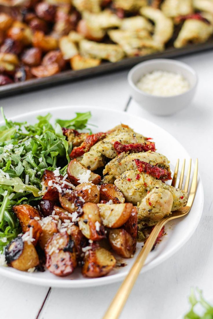 a white plate topped with meat and veggies next to a tray of food