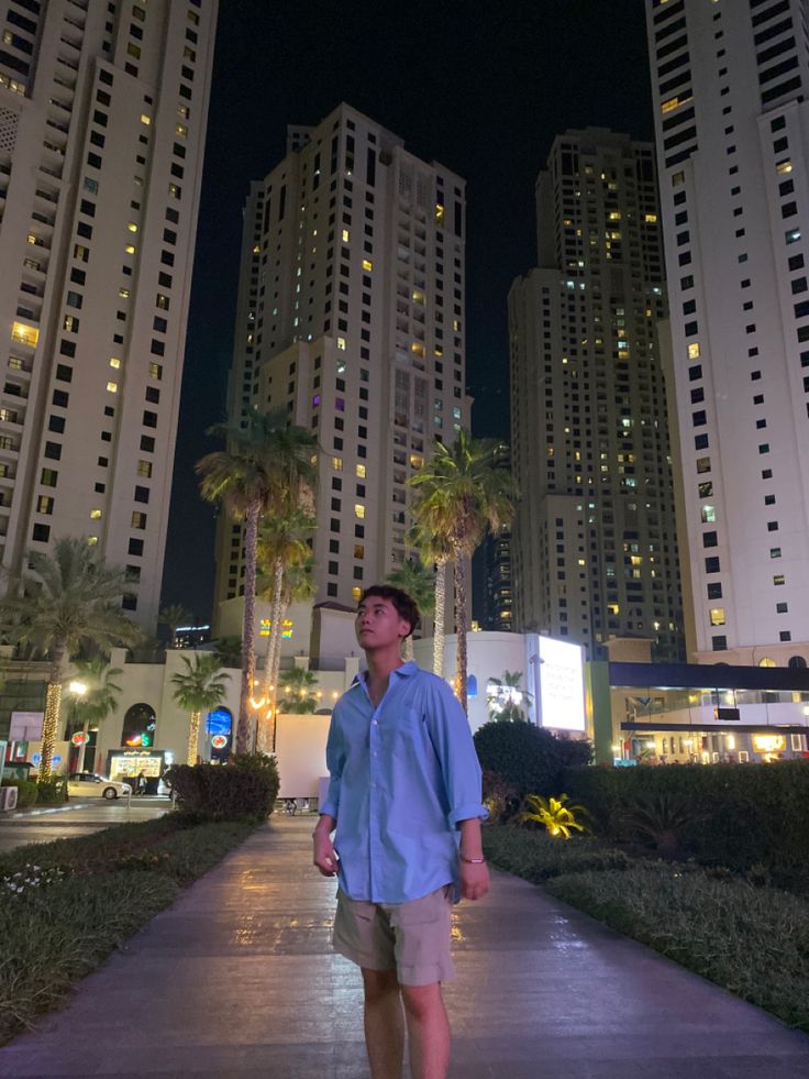 a man is walking down the sidewalk in front of tall buildings at night with palm trees