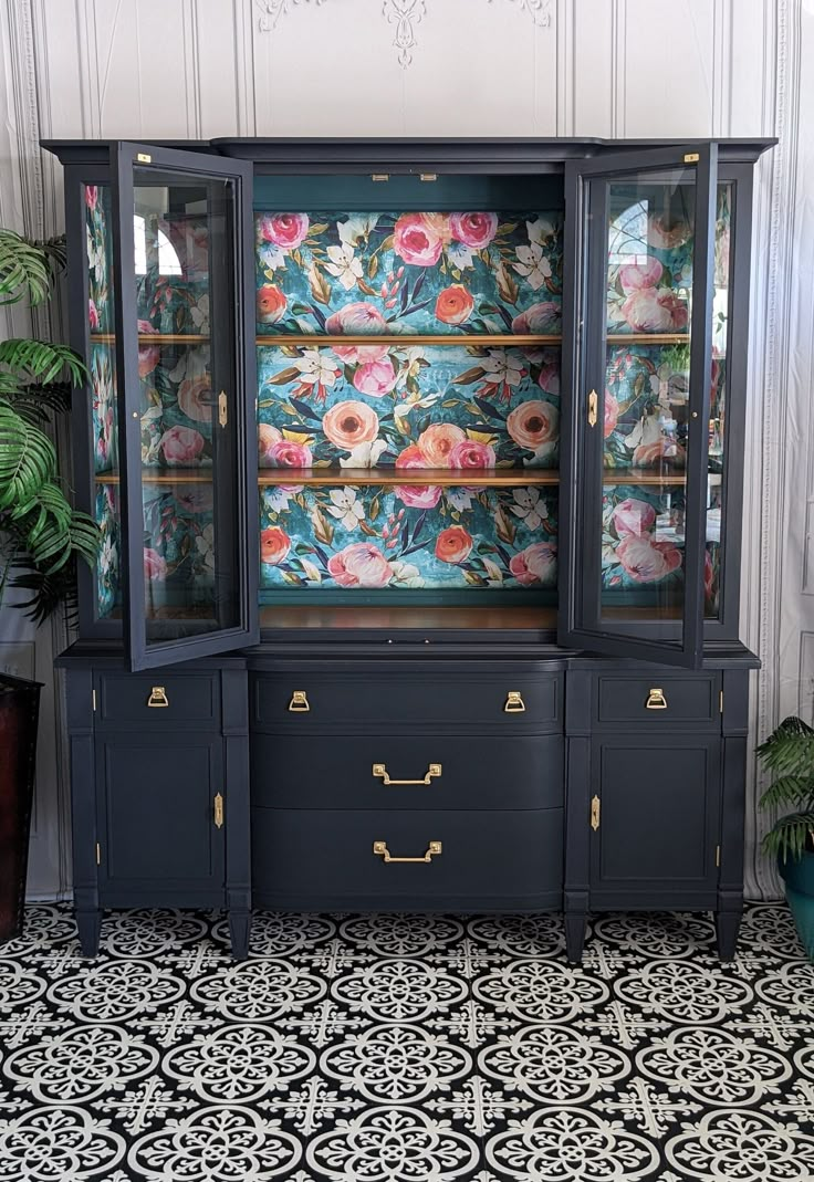 an antique china cabinet with floral wallpaper on the back and gold trimmings