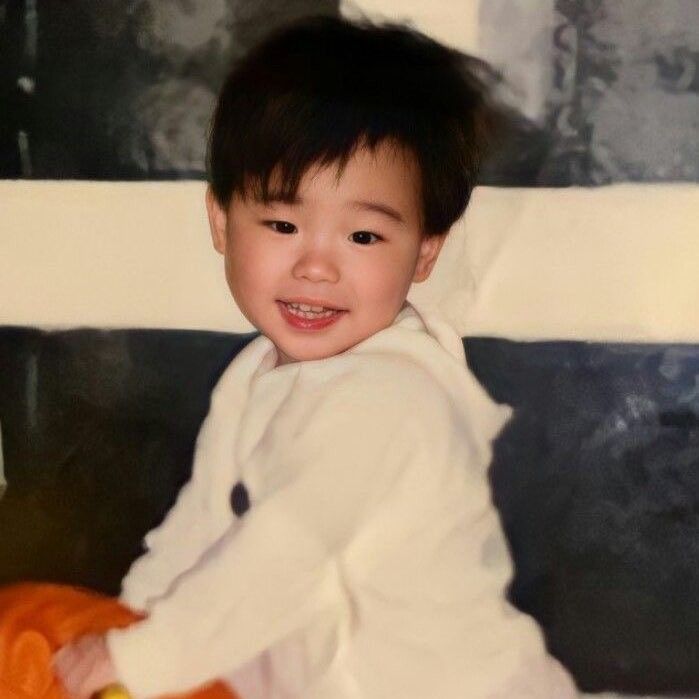 a young boy sitting on top of a bed next to a stuffed animal and smiling at the camera