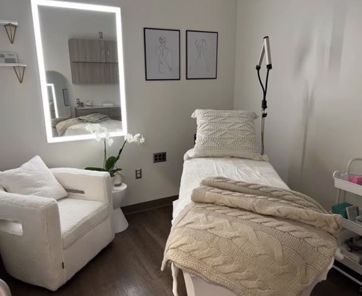 a white bed sitting in a bedroom next to a chair and mirror on the wall