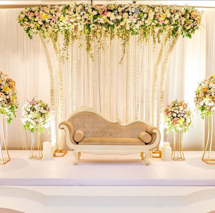 a couch sitting in front of a white stage with flowers on it and gold stands