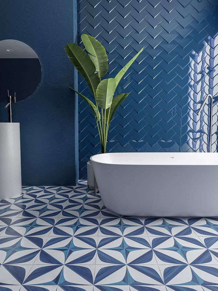 a white bath tub sitting next to a green plant in a blue tiled bathroom area