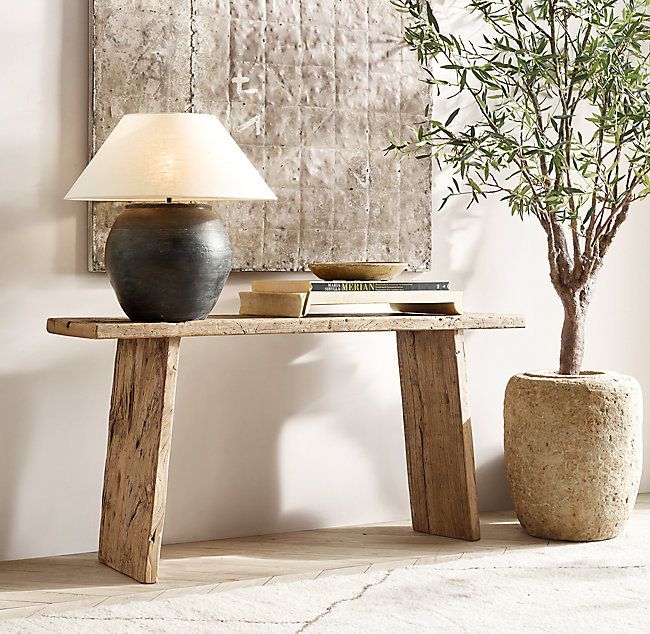 a table with a lamp and vase on it in front of a wall hanging art piece