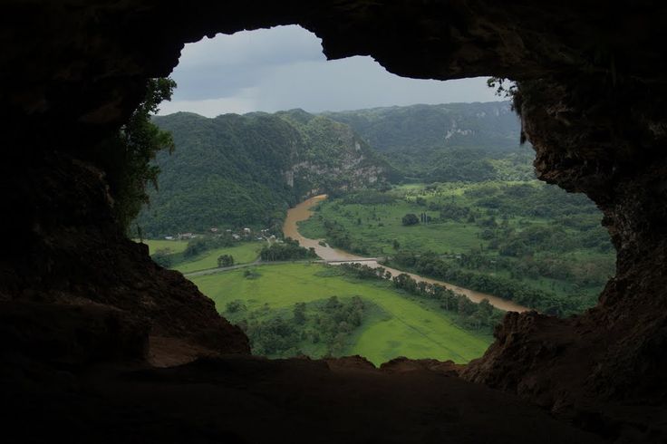 a view from the inside of a cave looking down on a river and mountains in the distance