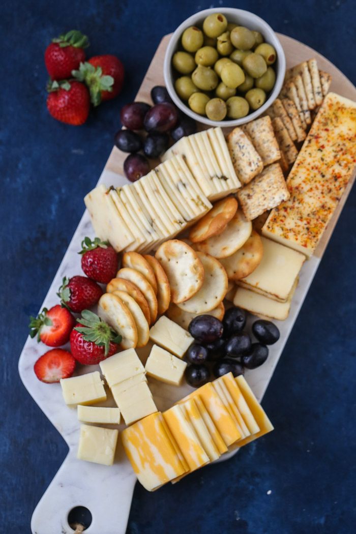 an assortment of cheeses, crackers and fruit on a cutting board