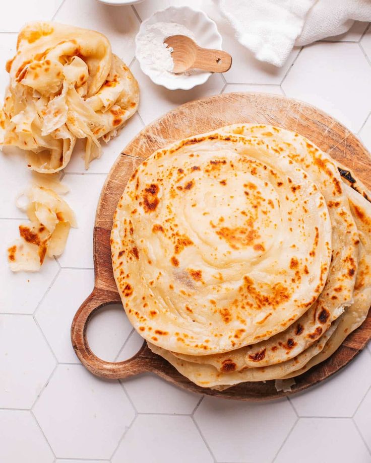 three flatbreads on a wooden plate with other food items around the bowl and spoon