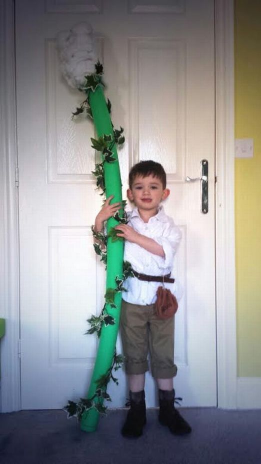 a young boy standing in front of a door holding onto a green pipe with ivy on it