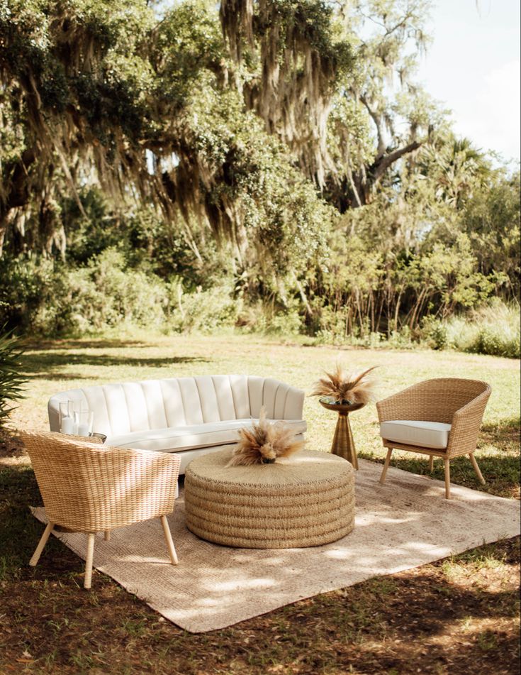 an outdoor seating area with two chairs and a round couch in the grass, surrounded by trees