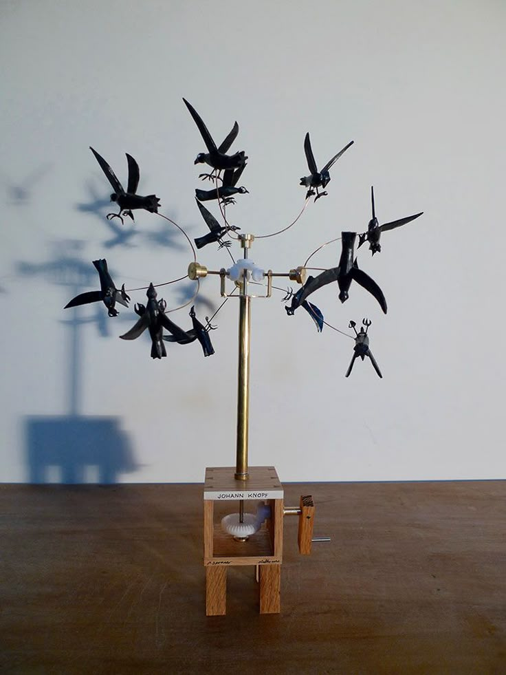 there is a sculpture made out of birds on top of a wooden table with a white wall in the background