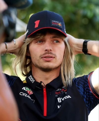 a man with long hair wearing a hat and holding his hands to his head while standing in front of a camera