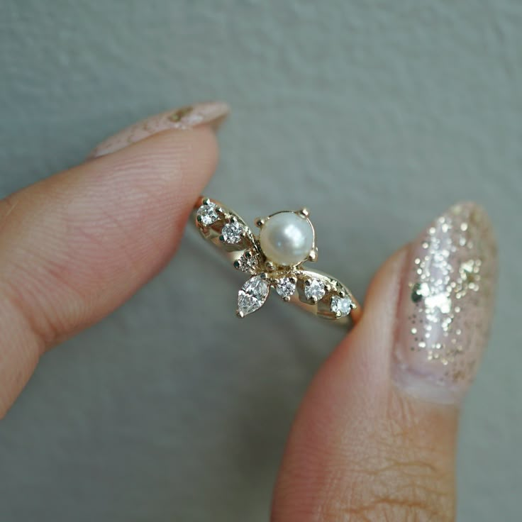 a close up of a person's hand holding a diamond and pearl ring