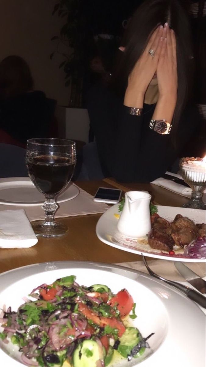 a woman sitting at a table in front of a plate of food with meat and vegetables on it