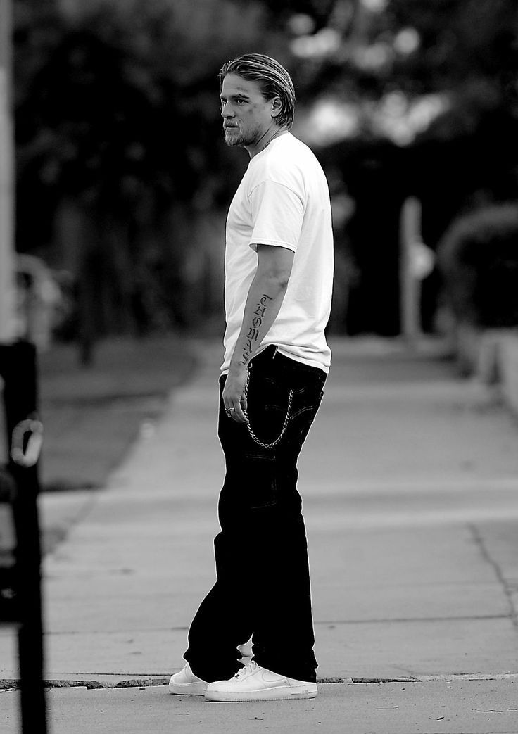 a man in white shirt and black pants standing on sidewalk next to parking meter with handbag