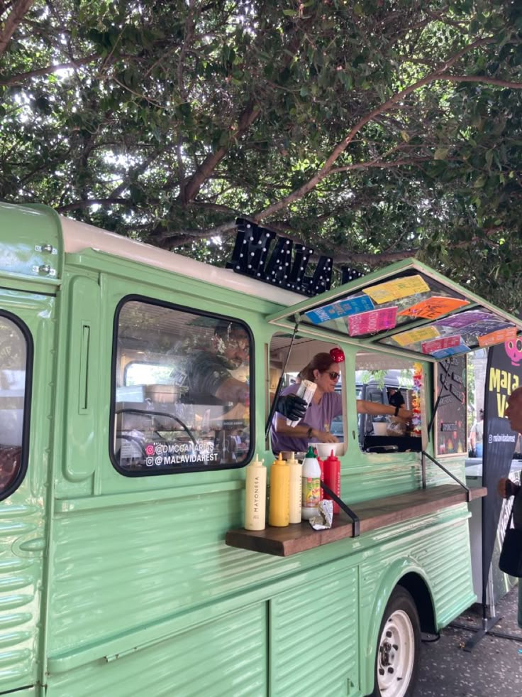 a green food truck parked next to a tree