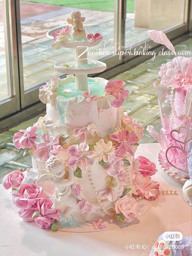 a three tiered cake is decorated with pink and white flowers on a table in front of a window