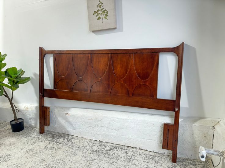 a wooden headboard sitting next to a potted plant in a room with white walls