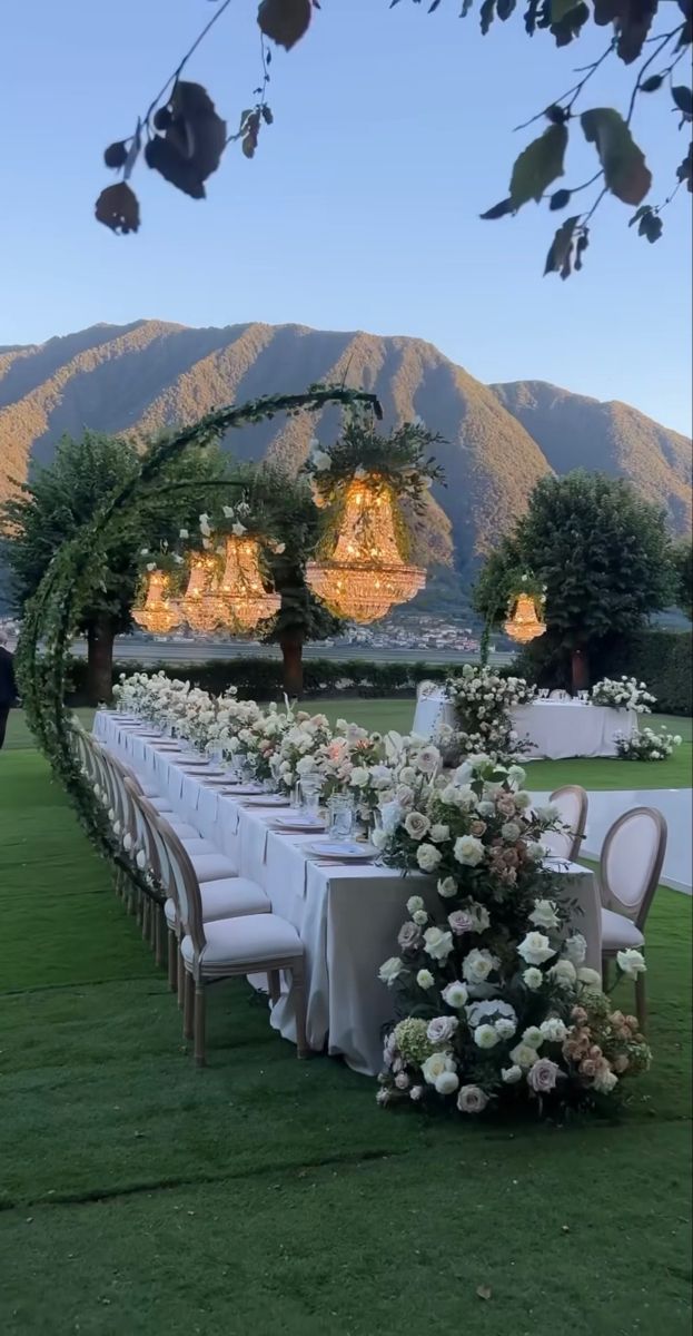 a long table set up with white flowers and greenery for an outdoor wedding reception