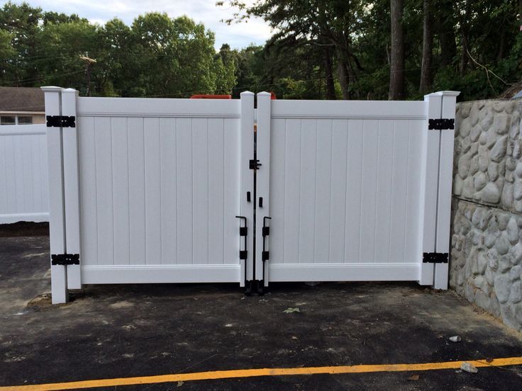 a white gate with black handles is open in front of a stone wall