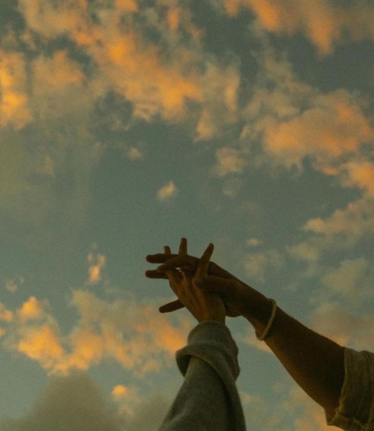 two people reaching up into the sky with their hands in the air and clouds behind them