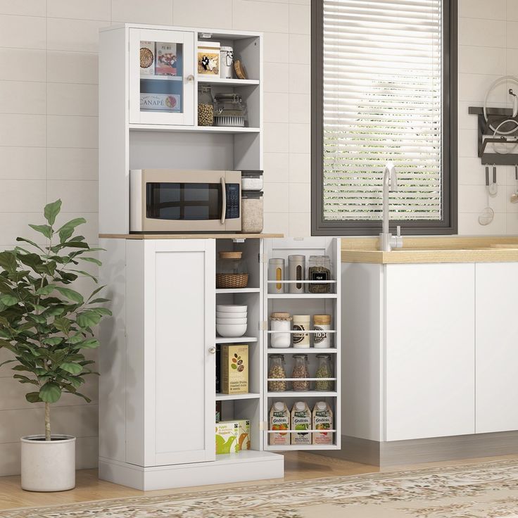 a kitchen with white cupboards and shelves filled with food on top of a wooden floor